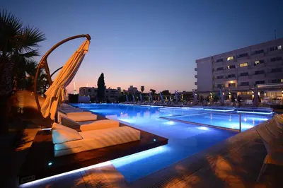 a large swimming pool with lounge chairs at night at Nestor Hotel in Ayia Napa