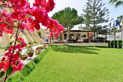 a green yard with pink flowers in front of a building at Napa Prince Hotel Apts in Ayia Napa