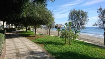 a walking path next to a beach with trees at Lordos Hotel Apts Limassol in Limassol