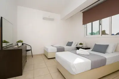 a bedroom with two beds and a desk and windows at Neraida - 2Bed Apart walk to Kalamies Beach in Protaras