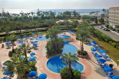 an overhead view of a resort pool with blue umbrellas and palm trees at Nissiana Hotel & Bungalows in Ayia Napa