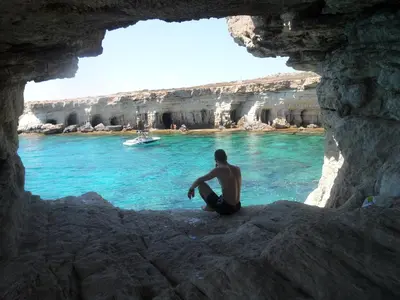 a man sitting on rocks in front of the water at SUNSHINE APTS, TWO BEDROOM , FREE INTERNET, No 3 in Ayia Napa