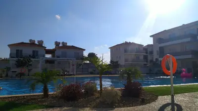 a swimming pool with palm trees in front of buildings at Amigos Apartment Mythical in Protaras
