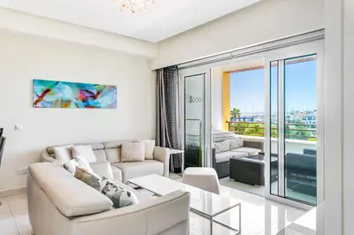 a living room with white furniture and a large window at Limassol Marina Nereids D22 by Ezoria Villas in Limassol