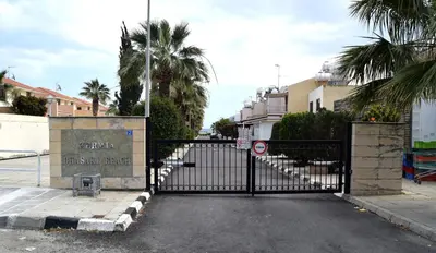 a black gate in a parking lot with palm trees at Christos beach house in Larnaka