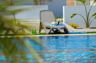 a person sitting in a chair next to a swimming pool at Mythical Sands Apartments in Protaras
