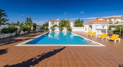 a swimming pool with chairs and a house at Mythical Sands Apartments in Protaras