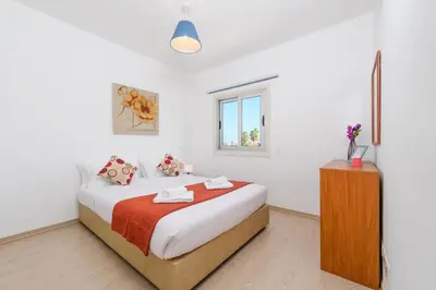 a white bedroom with a bed and a window at Ayia Triada View in Protaras
