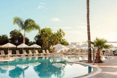 a swimming pool with lounge chairs and palm trees at Lantiana Gardens ApartHotel in Protaras