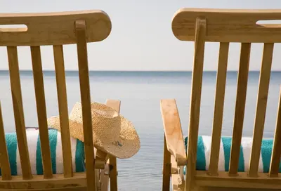 two chairs with a straw hat sitting next to the water at Sandy Beach Hotel & Spa - ex Sentido in Larnaka
