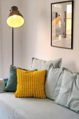 a yellow pillow on a gray couch with a mirror at City Rendezvous One Bedroom Flat in Larnaka