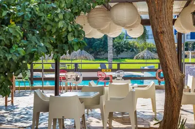 a restaurant with white tables and chairs and a pool at Captain Karas Holidays Apartments in Protaras