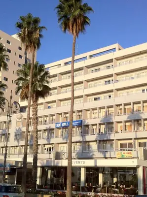 a large white building with palm trees in front of it at Sun Hall Beach Hotel Apartments in Larnaka