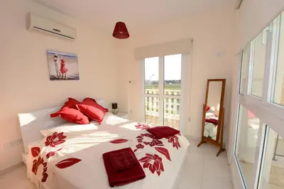 a white bedroom with a bed with red pillows at Karythia in Pyla