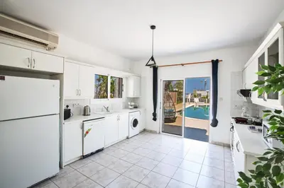 a kitchen with white cabinets and a view of a pool at Jason Villas in Protaras