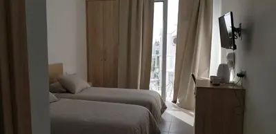 a bedroom with two beds and a television and a window at Sunny Napa Apartments in Ayia Napa