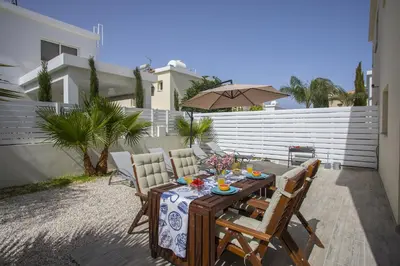 a table with chairs and an umbrella on a patio at Protaras Galleria Sunset Villa in Paralimni