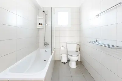 a white bathroom with a toilet and a bath tub at Villa Palm Breeze by Ezoria Villas in Protaras