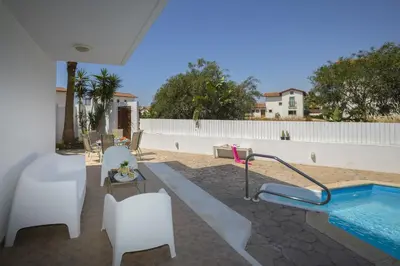 a patio with a swimming pool and white chairs at Villa Serene in Ayia Napa