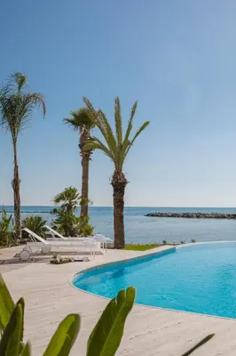 a swimming pool with palm trees and the ocean at Lebay Beach Hotel in Larnaka
