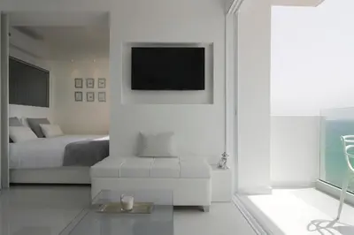 a white bedroom with a bed and a tv at The White Pearl Suite - beach front city centre with sea view. in Limassol