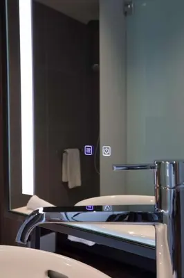 a mirror in a bathroom with a chair in front of a sink at Radisson Blu Hotel, Larnaca in Larnaka