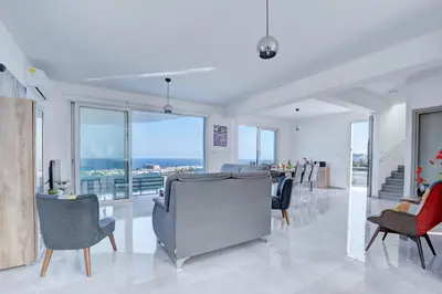 a living room with chairs and tables and windows at Aetopetra Villa in Protaras