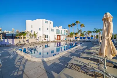 a pool at a resort with chairs and an umbrella at Protaras Plaza Hotel in Protaras