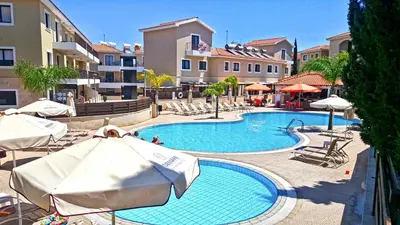 a swimming pool with umbrellas and chairs and buildings at Kapparis town house in Paralimni