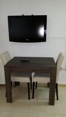 a wooden table with chairs and a television on a wall at Agrino Hotel Apartments in Ayia Napa