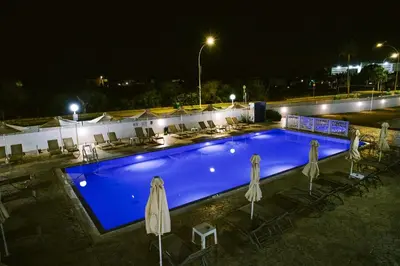 a swimming pool at night with chairs and umbrellas at Kaos Hotel Apartments in Ayia Napa