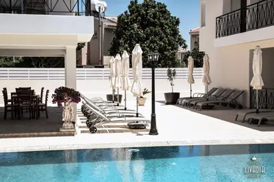 a pool with chairs and umbrellas next to a building at Carisa Livadia Gardens in Livadhia