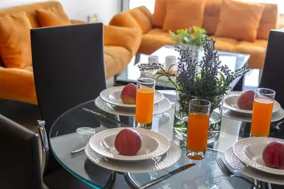 a glass table with plates of fruit and orange juice at one bedroom apartment in Fig tree bay in Protaras