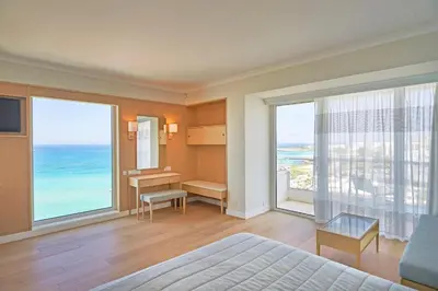 a bedroom with a bed and a desk and windows at Sunrise Beach Hotel in Protaras