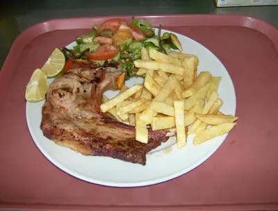 a plate of food with a piece of meat and french fries at Rantzo Holiday Apartments in Pissouri