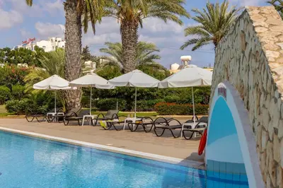 a swimming pool with chairs and umbrellas and a surfboard at Seagull Hotel Apartments in Protaras