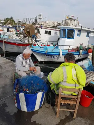 two men are sitting in chairs next to a boat at Haig's Dream Flat On The Beach in Larnaka