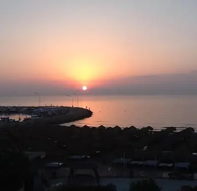 a sunset over a body of water with the sun setting at Haig's Dream Flat On The Beach in Larnaka