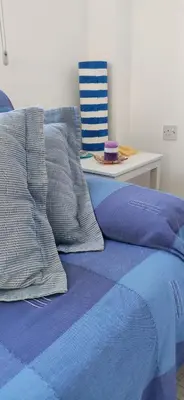 a bed with blue sheets and pillows next to a table at Cozy holyday apartament in Paralimni