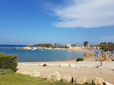 a beach with blue chairs and boats in the water at Cozy holyday apartament in Paralimni