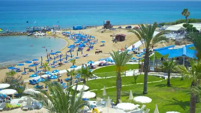a beach with blue and white umbrellas and the ocean at MyroAndrou Beach Hotel Apartments in Protaras