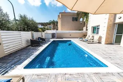 a swimming pool with an umbrella next to a house at Timotheos Villa in Protaras