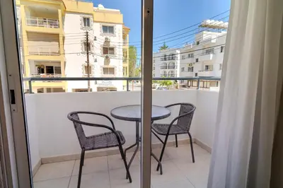 a table and chairs on a balcony with a window at Helios Mackenzie One Bedroom Flat in Larnaka