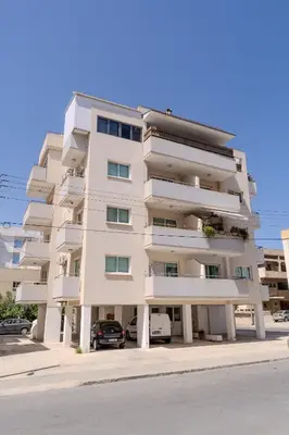 a white apartment building with cars parked in front of it at Helios Mackenzie One Bedroom Flat in Larnaka