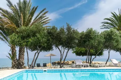 a swimming pool with palm trees and the ocean at Elya Beach Luxury Suites in Ayios Theodhoros