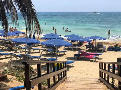 a beach with blue umbrellas and people in the water at Ayia Napa GO SEA Sunny Apt with Terrace 5 min to Beach in Ayia Napa