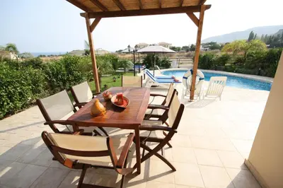 a wooden table and chairs on a patio with a pool at Holidays Villas in Pissouri