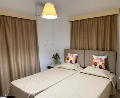 two beds in a bedroom with curtains and flowers at Terpsithea Apartments in Ayia Napa