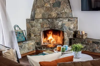 a stone fireplace in a living room with a table at Platres Forest View Cottage in Platres