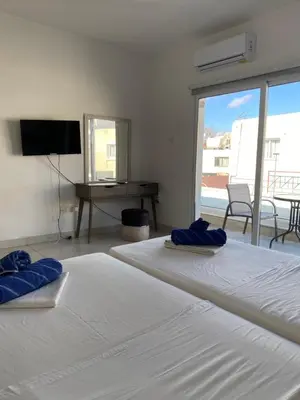 two beds in a room with a television and a desk at Midtown Napa Apartments in Ayia Napa